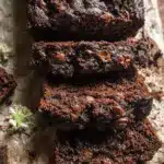 Deliciously moist double chocolate chip zucchini bread slice on a wooden table, garnished with chocolate chips and powdered sugar.
