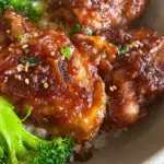 Plated easy soy garlic chicken thighs garnished with sesame seeds and green onions, served with rice and vegetables.