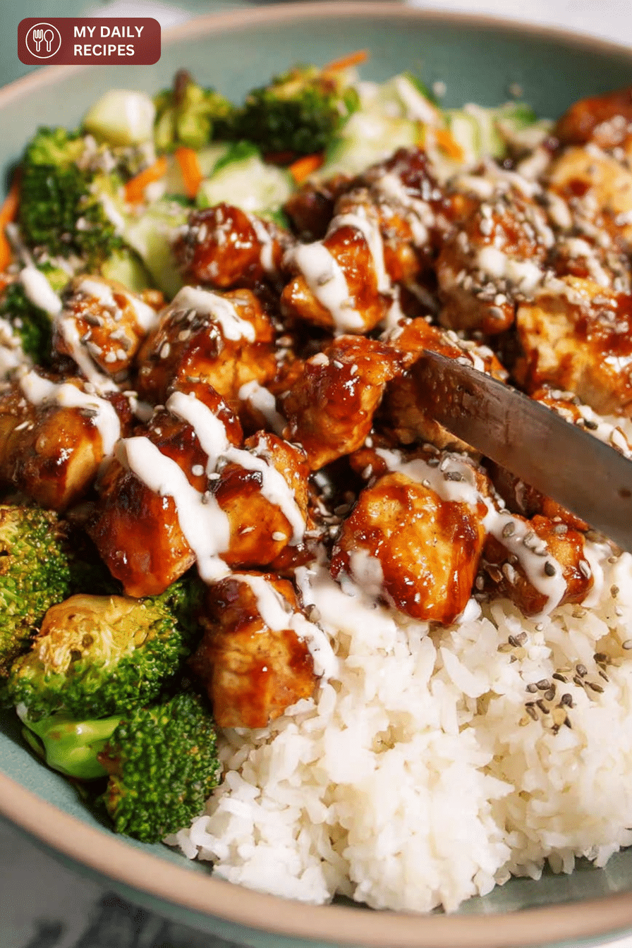 Close up of sticky chicken bowl with sesame seeds, green onions, tender chicken, and broccoli on rice.