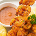 Close-up of perfectly cooked air fryer shrimp garnished with parsley and lemon wedges.