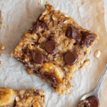Delicious banana oatmeal bars stacked on a rustic wooden plate with fresh bananas and oats.