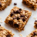 Close-up of sliced banana peanut butter oatmeal bars on a cutting board with peanut butter drizzle and chocolate chips