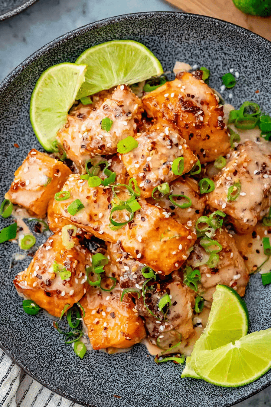 Plated Bang Bang Salmon with sauce, lime wedges, and fresh herbs