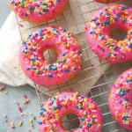 Close-up of a vibrant birthday cake doughnut with colorful sprinkles on a decorated table.