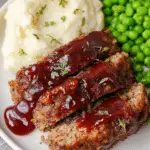 Sliced brown sugar glazed meatloaf on a wooden cutting board, garnished with rosemary.