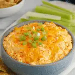 A delicious buffalo chicken dip in a crock pot garnished with green onions, with tortilla chips and fresh veggies on the side.
