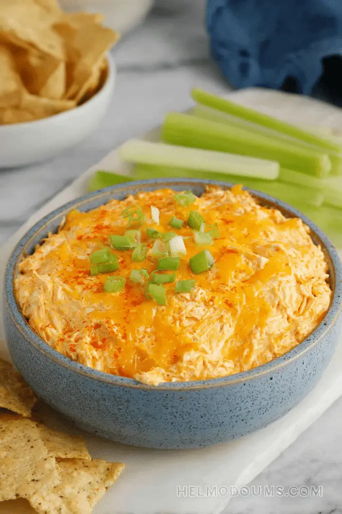 A delicious buffalo chicken dip in a crock pot garnished with green onions, with tortilla chips and fresh veggies on the side.