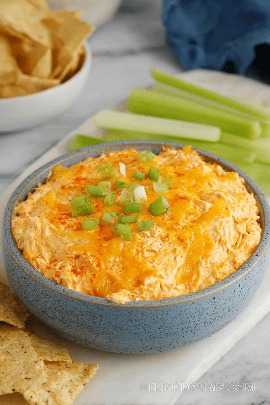 A delicious buffalo chicken dip in a crock pot garnished with green onions, with tortilla chips and fresh veggies on the side.