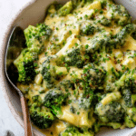 Delicious close-up of cheesy broccoli with melted cheddar and Parmesan cheese, garnished with herbs.