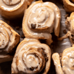 Delicious coffee rolls with cream cheese frosting on a wooden table, surrounded by coffee beans.