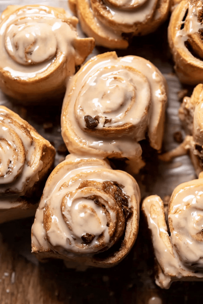Delicious coffee rolls with cream cheese frosting on a wooden table, surrounded by coffee beans.