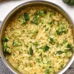 Close-up of creamy broccoli cheddar orzo in a rustic bowl, garnished with fresh herbs.