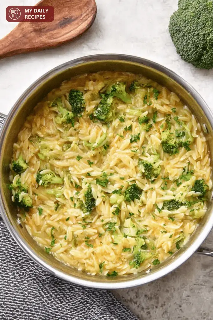 Close-up of creamy broccoli cheddar orzo in a rustic bowl, garnished with fresh herbs.
