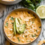 Bowl of creamy white chicken chili with cilantro and avocado, served with tortilla chips.