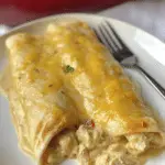 Close-up of creamy white chicken enchiladas with melted cheese and green chiles in a baking dish.