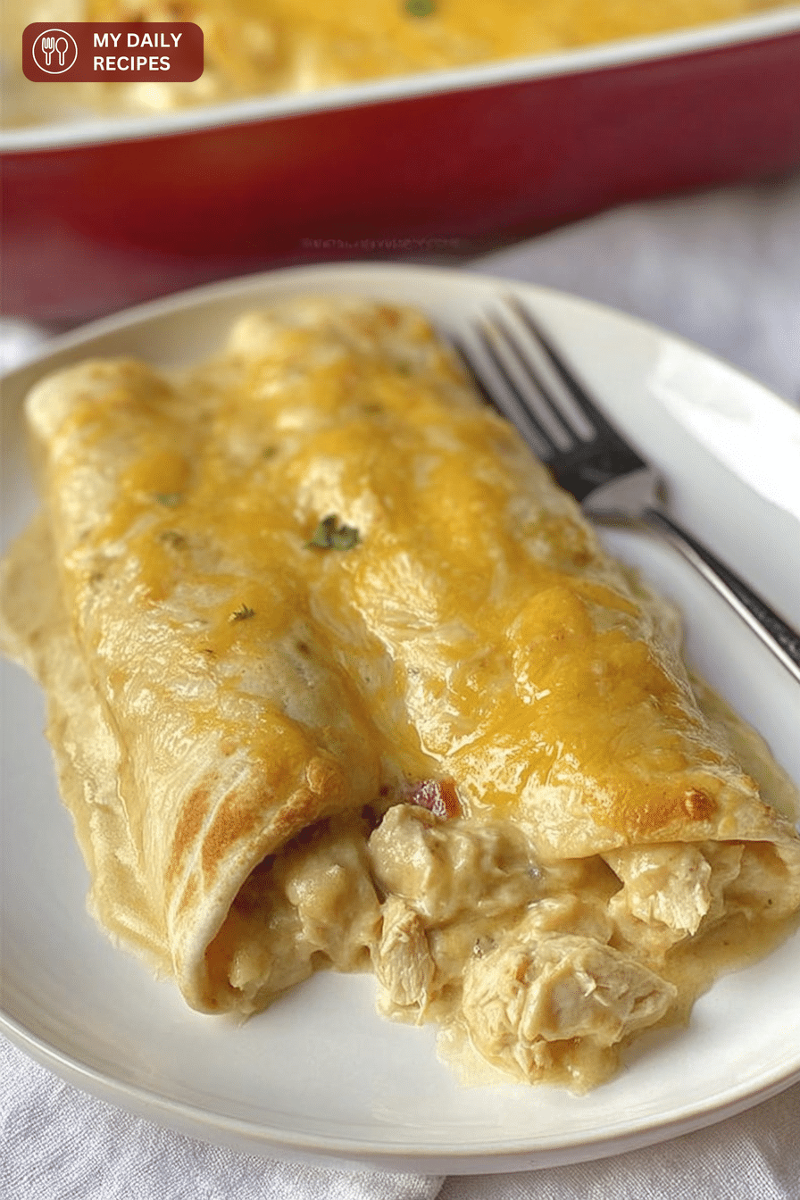 Close-up of creamy white chicken enchiladas with melted cheese and green chiles in a baking dish.