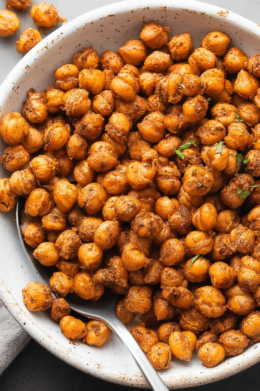 Crispy roasted chickpeas in a white bowl with Mediterranean garnishes, perfect for a healthy snack.