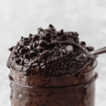 Close-up of creamy edible brownie batter in a bowl with chocolate chips and a wooden spoon.