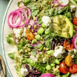 Vibrant Everything Spring Green Salad with colorful cherry tomatoes, cucumbers, and a drizzle of lemon basil vinaigrette on a wooden table.
