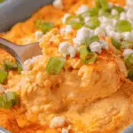 A colorful bowl of buffalo chicken dip surrounded by tortilla chips, garnished with fresh herbs and cheese.