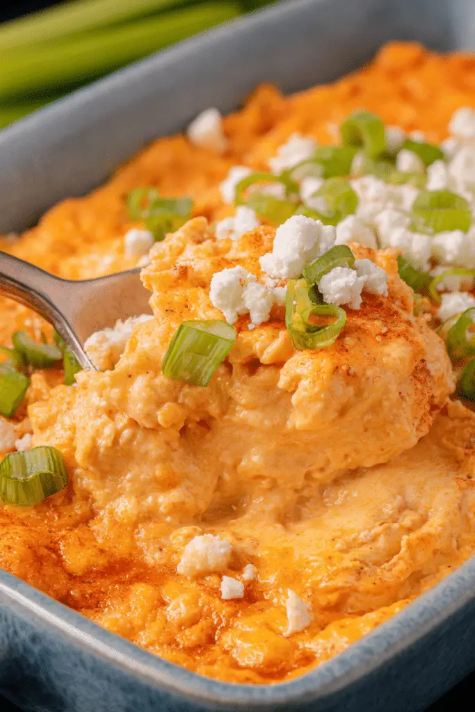 A colorful bowl of buffalo chicken dip surrounded by tortilla chips, garnished with fresh herbs and cheese.