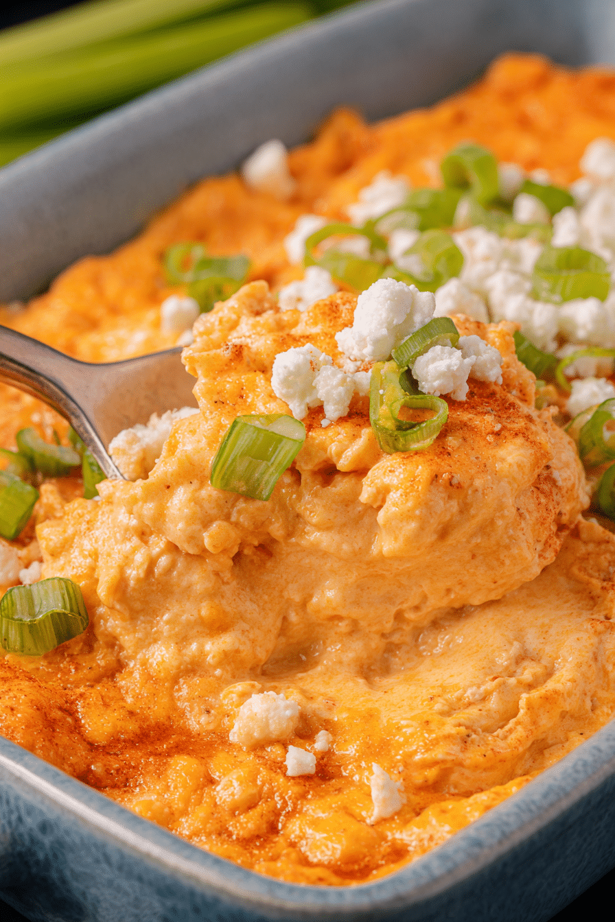 A colorful bowl of buffalo chicken dip surrounded by tortilla chips, garnished with fresh herbs and cheese.
