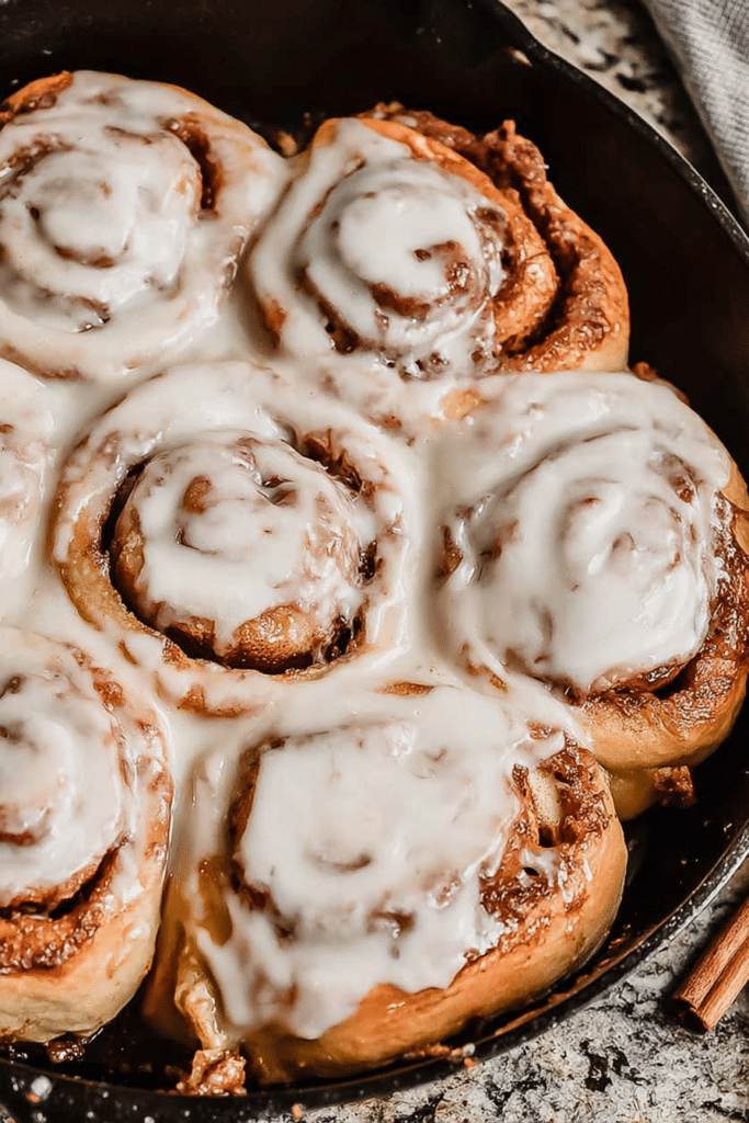 Freshly baked sourdough cinnamon rolls with a creamy glaze on a wooden table.