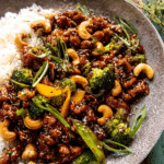 Close-up of garlic butter cashew chicken with rice, garnished with green onions and sesame seeds.