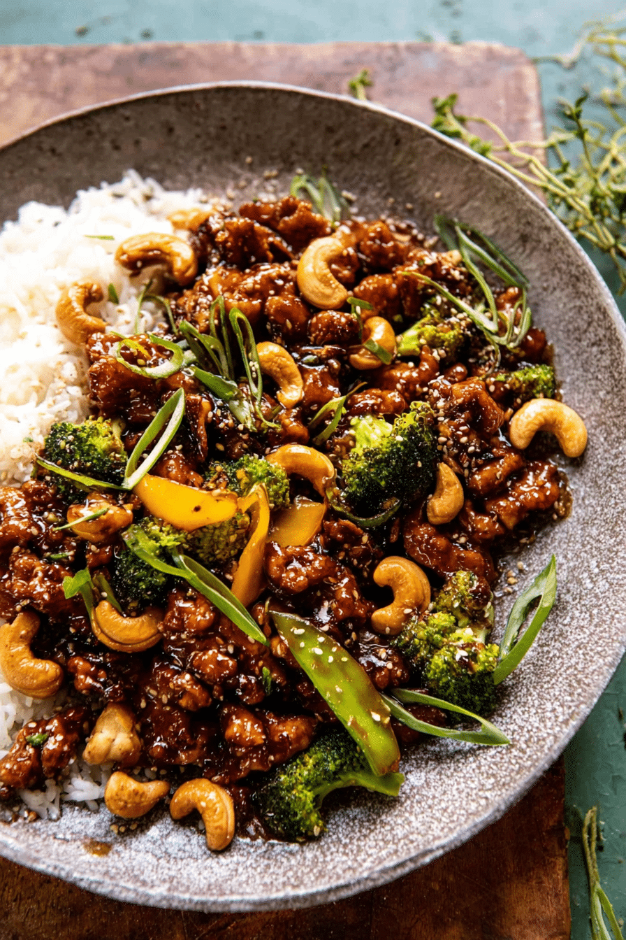 Close-up of garlic butter cashew chicken with rice, garnished with green onions and sesame seeds.