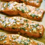 Delicious garlic butter salmon garnished with fresh parsley and lemon wedges on a wooden table.