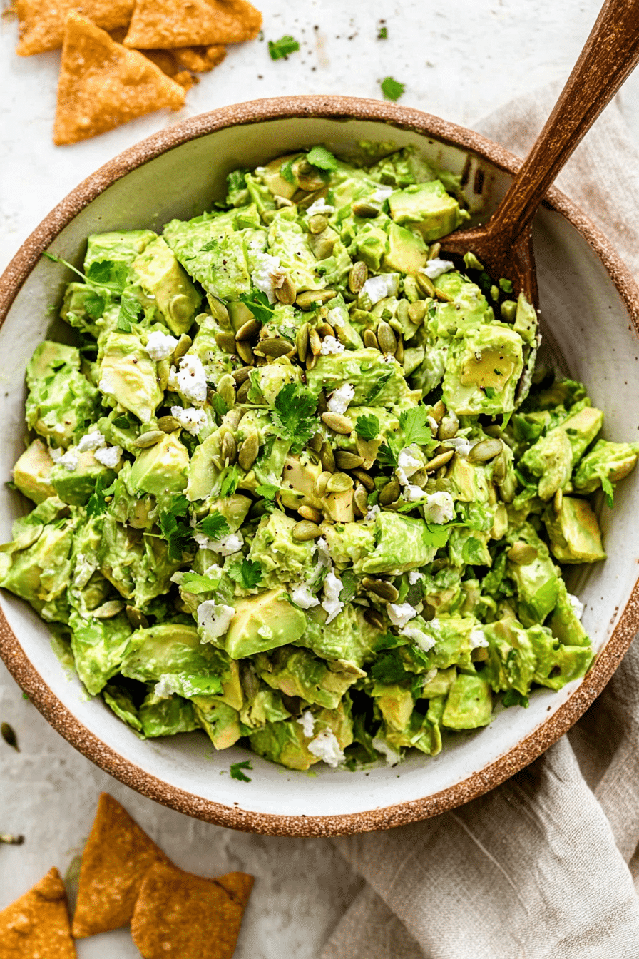 A bowl of green goddess salad filled with cabbage, avocado, cucumber, green onions, and feta cheese, with chips for serving.