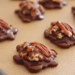 Delicious homemade turtles candy with caramel and chocolate, garnished with pecans on a white plate.