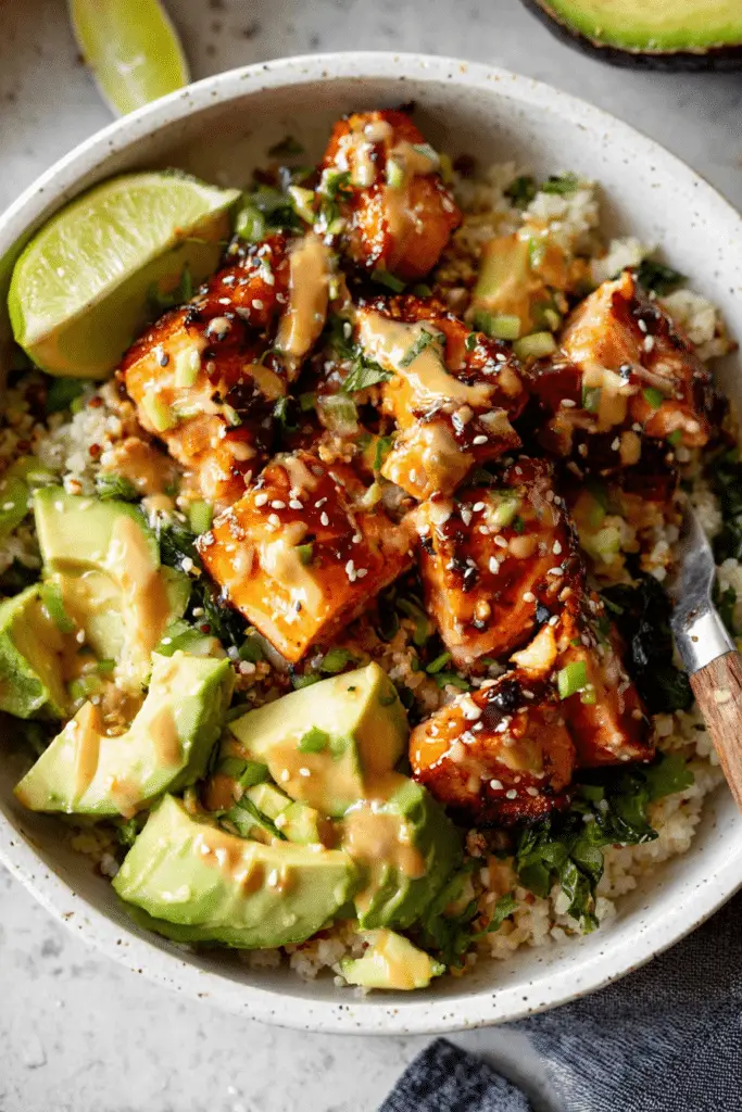 Honey glazed salmon rice bowl with avocado and cucumber on a wooden table
