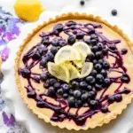 Lemon blueberry tart served on a plate with lemon slices and blueberries on a wooden table.