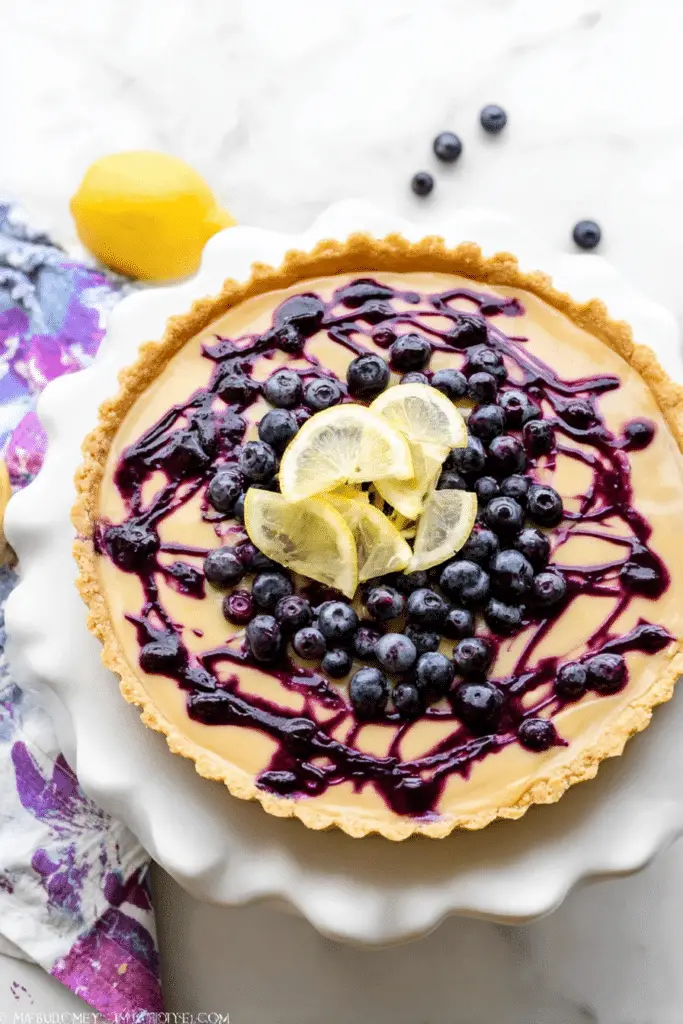 Lemon blueberry tart served on a plate with lemon slices and blueberries on a wooden table.