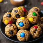Close-up of homemade quick monster cookie protein balls with chocolate chips and colorful candies on a wooden board.