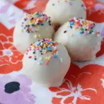 Colorful no-bake cake batter truffles topped with sprinkles on a white plate.