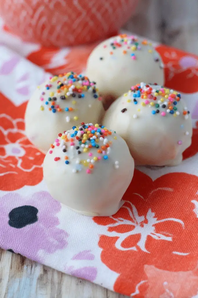 Colorful no-bake cake batter truffles topped with sprinkles on a white plate.