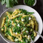 Pea pasta with fresh mint and truffle oil served in a bowl with lemon zest on a wooden table.