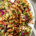 Colorful sesame chicken salad with grilled chicken, cabbage, and almonds on a wooden table.