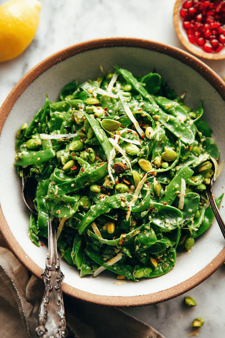 Vibrant snap pea salad with fresh basil and roasted pistachios in a rustic wooden bowl