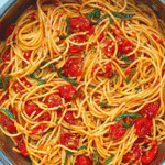 A delicious plate of spicy spaghetti adorned with fresh basil, cherry tomatoes, and parmesan on a wooden table.