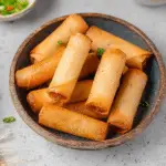 Crispy vegan Filipino spring rolls served on a plate with various dipping sauces.