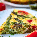 Close-up of a delicious asparagus frittata topped with cherry tomatoes and green onions on a wooden table.