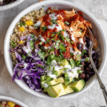 Delicious BBQ ranch chicken quinoa bowl filled with colorful ingredients including avocado, black beans, and red cabbage.