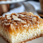 Slice of Bienenstich cake showcasing the creamy filling and almond topping, served on a wooden table.