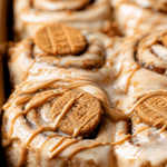 Delicious homemade Biscoff cinnamon rolls with cream cheese icing and crushed cookies on top, served on a rustic wooden table.