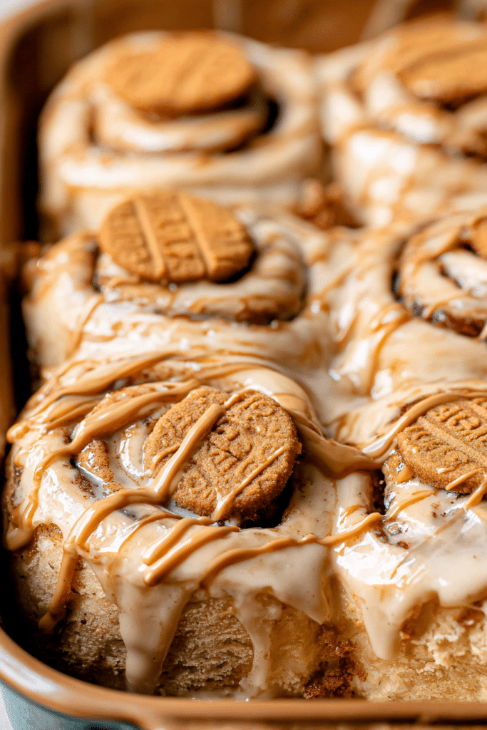 Delicious homemade Biscoff cinnamon rolls with cream cheese icing and crushed cookies on top, served on a rustic wooden table.