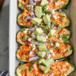 Buffalo chicken zucchini boats topped with ranch dressing and garnished with cilantro and red onion.