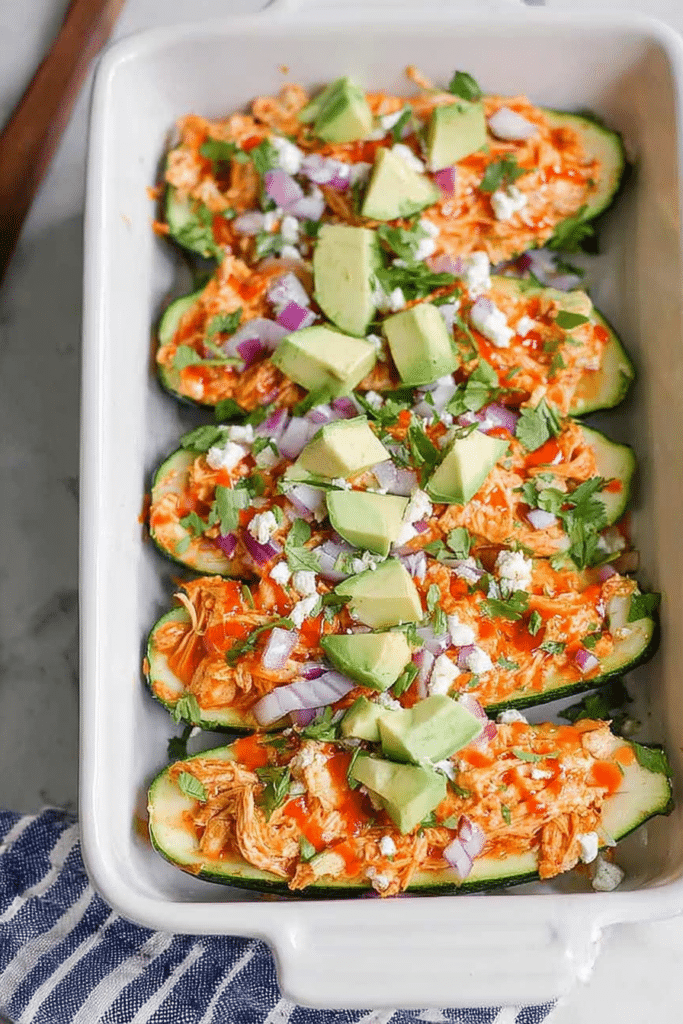 Buffalo chicken zucchini boats topped with ranch dressing and garnished with cilantro and red onion.